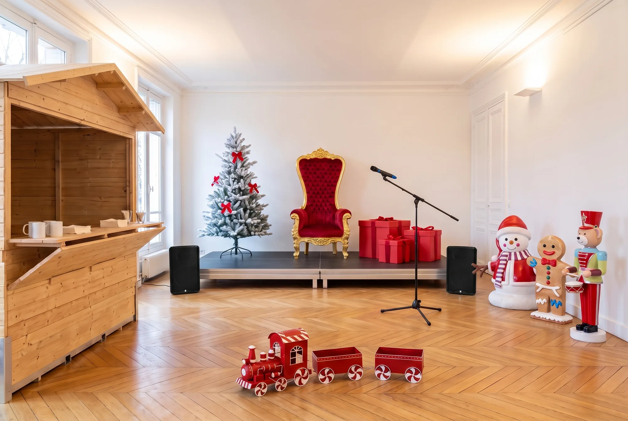 Salle préparée pour l'arbre de Noël d'une entreprise : petite scène avec trône rouge et or, sapin enneigé et cadeaux, enceintes et micro sur pied, chalet en bois pour le goûter, bonhomme de neige, bonhomme pain d'épice, ourson tambour et petit train rouge