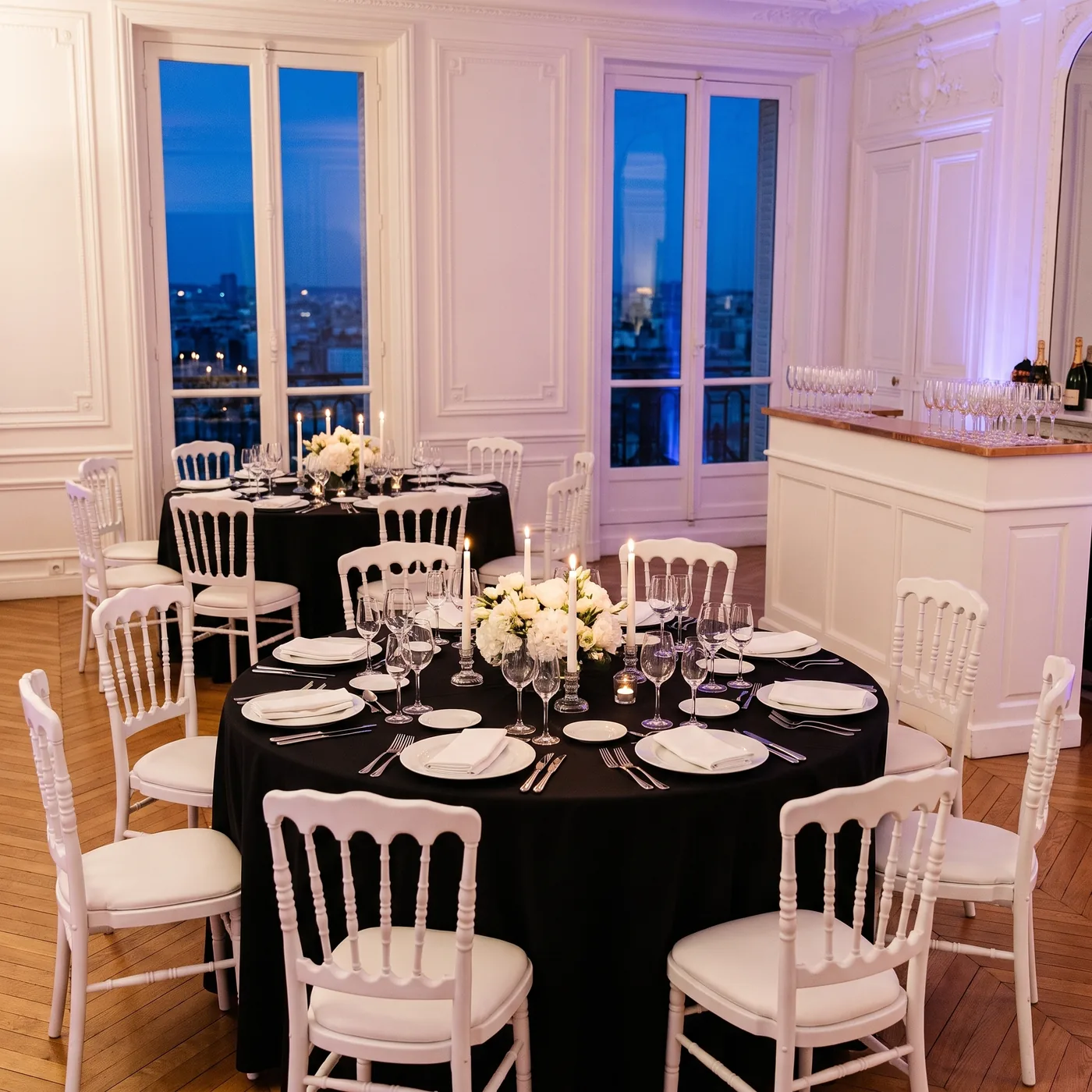 Dîner de réception dressé : tables rondes à nappe noire, chaises Napoléon III blanches et bar blanc