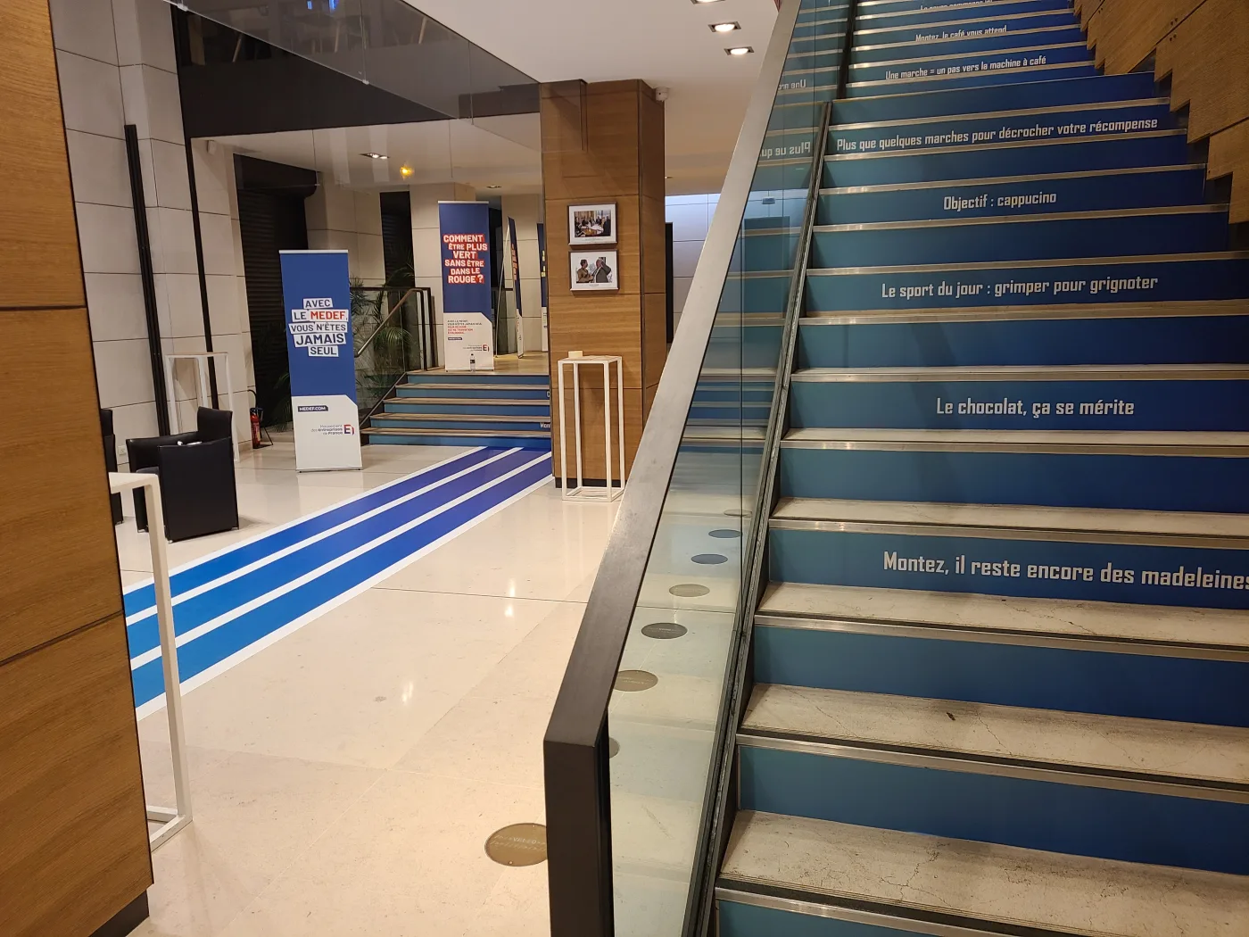 Contremarches de l'escalier imprimées avec des messages, prolongées par le parcours bleu au sol