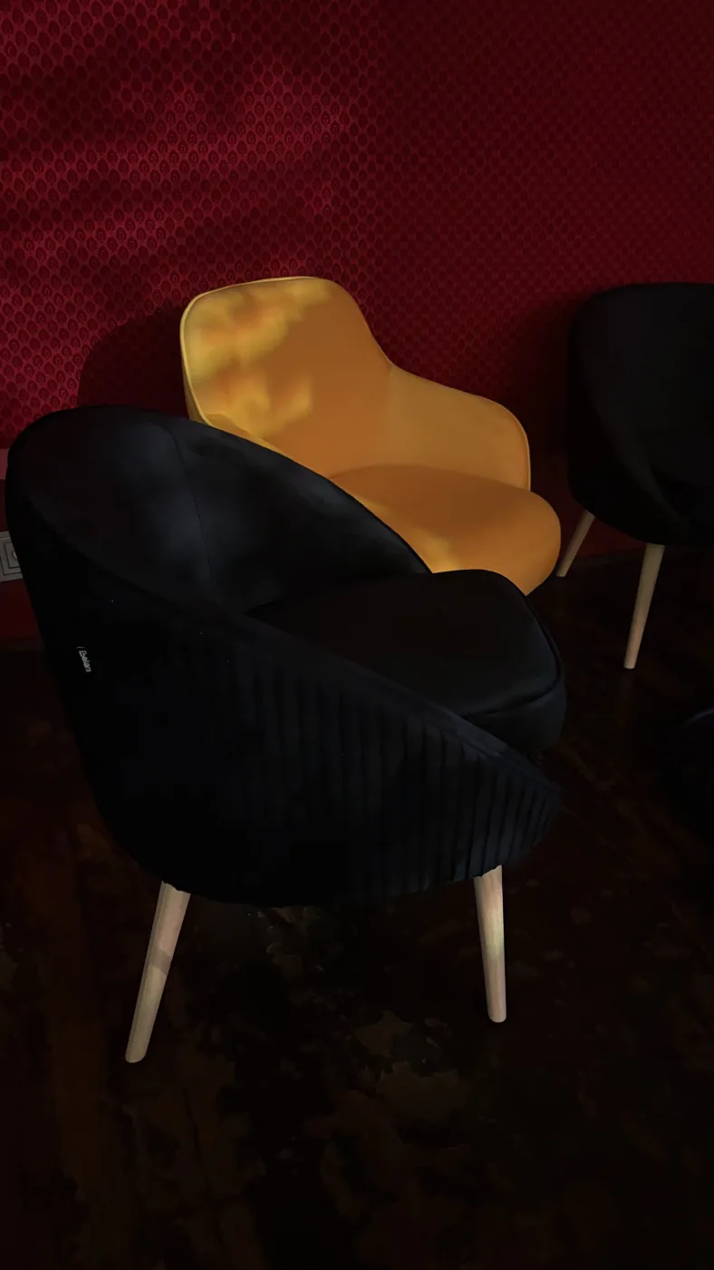 Fauteuil en velours jaune entouré de fauteuils noirs, devant un mur rouge de la salle